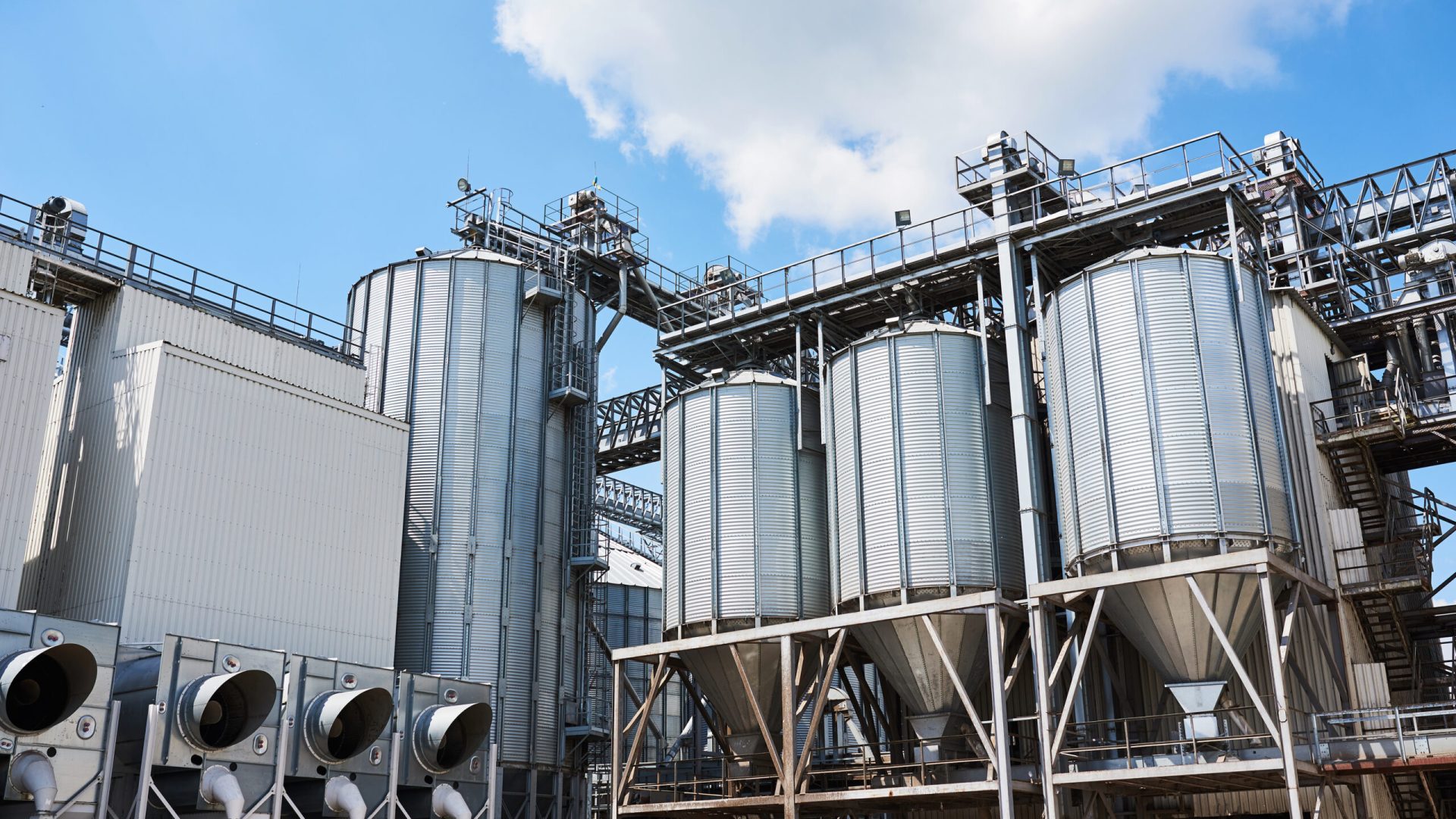 Agricultural Silos. Building Exterior. Storage and drying of grains, wheat, corn, soy, sunflower against the blue sky with white clouds.